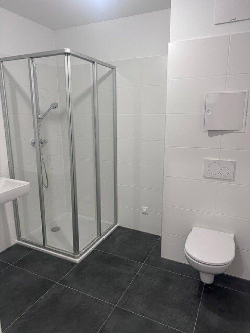 Modernes Badezimmer mit Duschkabine, wandhängendem WC und dunklen Bodenfliesen.