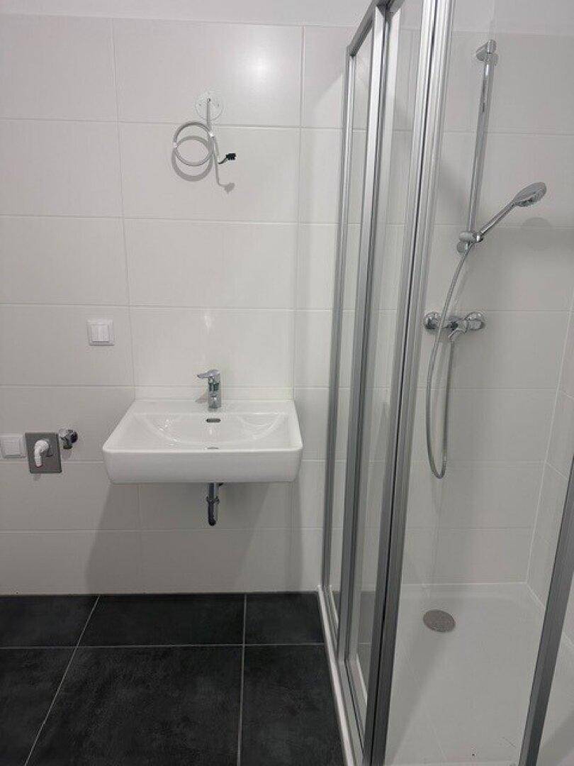 Detailansicht des Badezimmers mit Waschbecken, Duschkabine und weißen Wandfliesen.