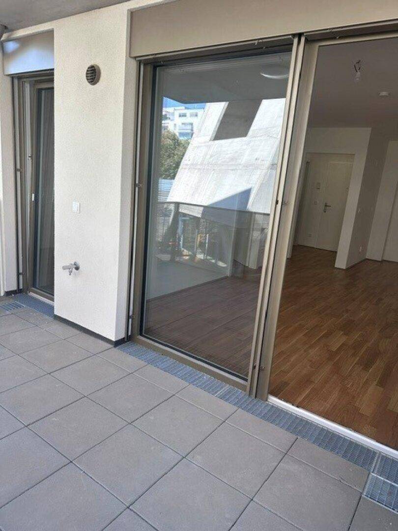 Blick vom gefliesten Balkon in den hellen Innenraum mit Holzboden.