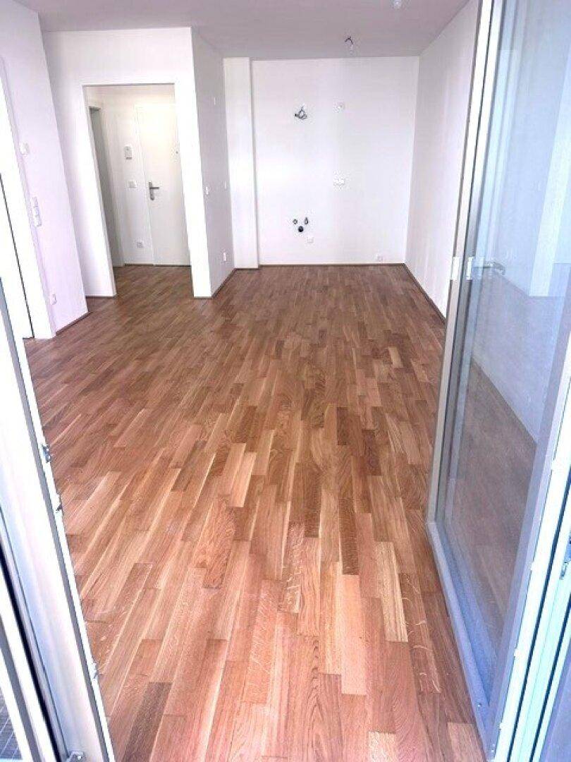 Geräumiger, leerer Raum mit Holzboden und Zugang zu einem Außenbereich.