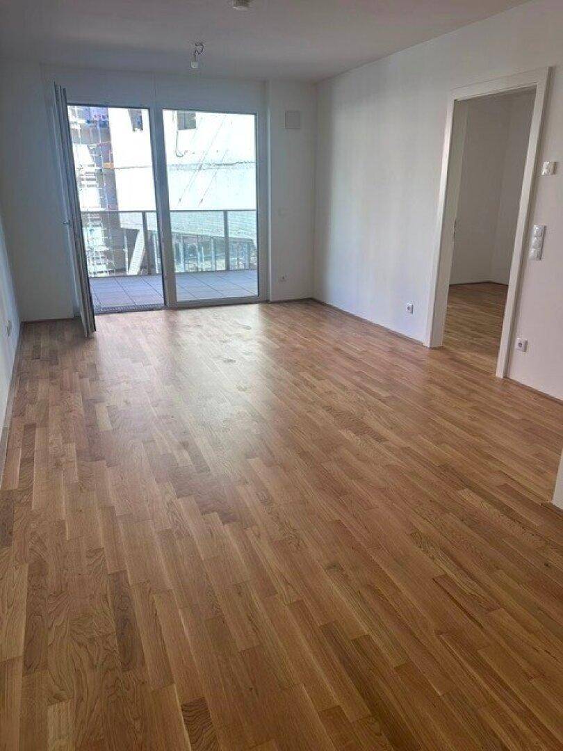 Heller Wohnraum mit Holzboden und großen Fenstern, die viel Tageslicht hereinlassen.