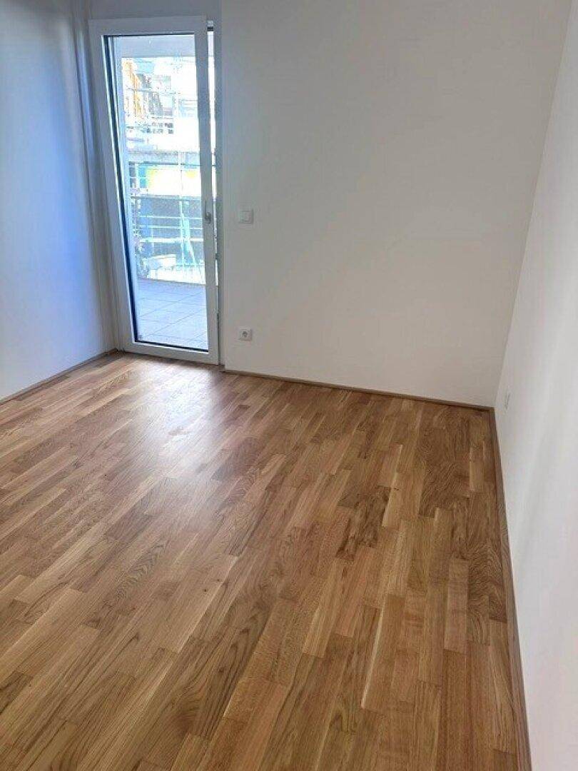 Helles Schlafzimmer mit Holzboden und direktem Zugang zu einem Balkon.