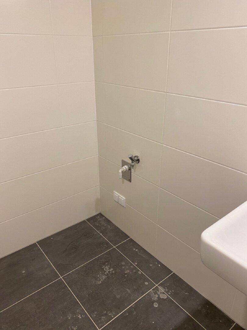 Ecke eines Badezimmers mit Fliesen und vorbereiteten Anschlüssen für eine Toilette.
