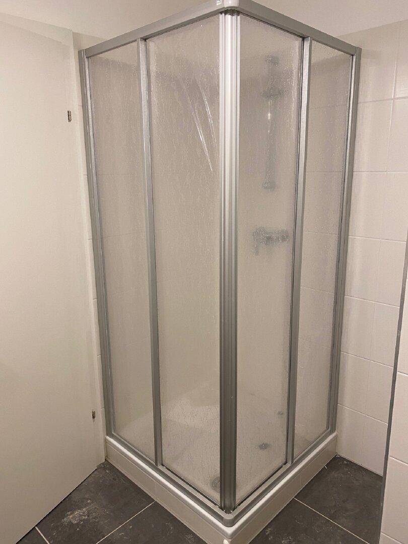 Eckduschkabine mit Milchglas und Fliesen an Wänden und Boden in einem modernen Badezimmer.