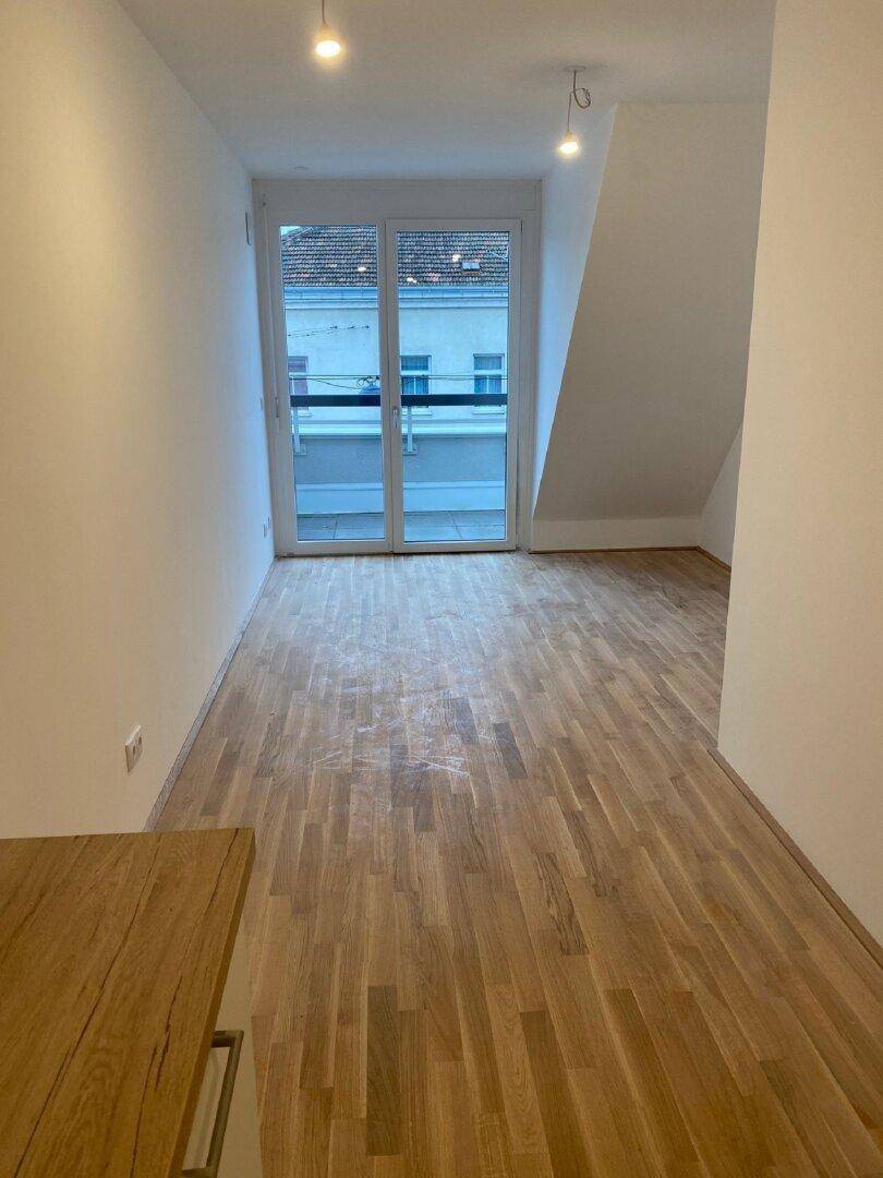 Heller Wohnraum mit Holzboden, Dachschräge und Zugang zu einem Balkon durch eine große Glastür.