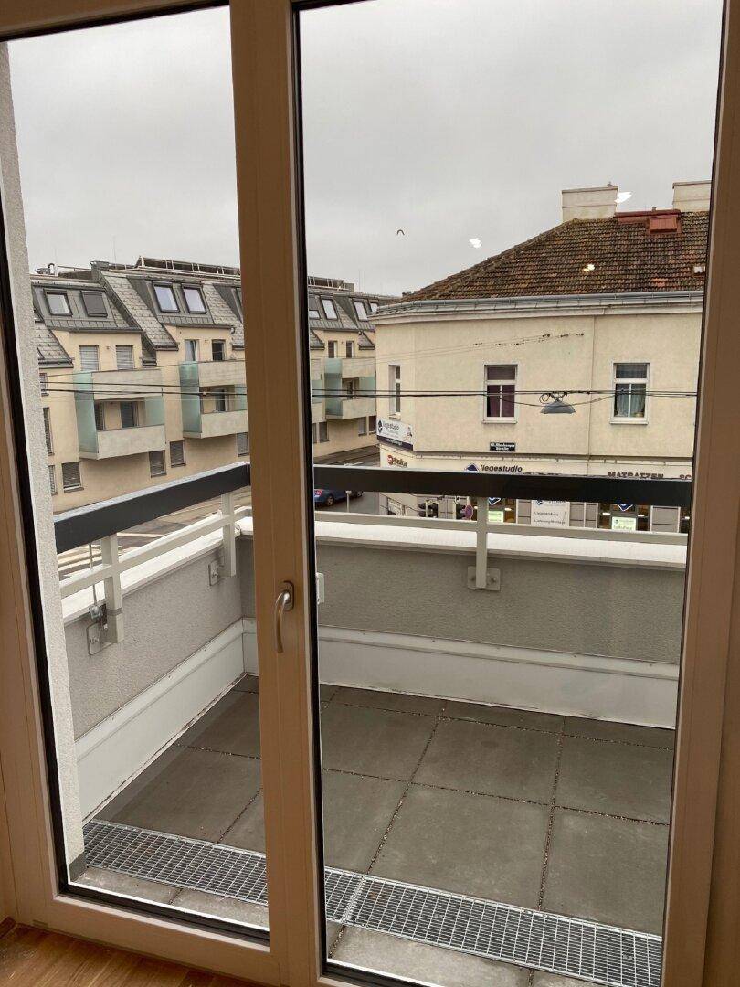Blick vom Innenraum auf einen gefliesten Balkon mit Geländer und die umliegende Stadtbebauung.