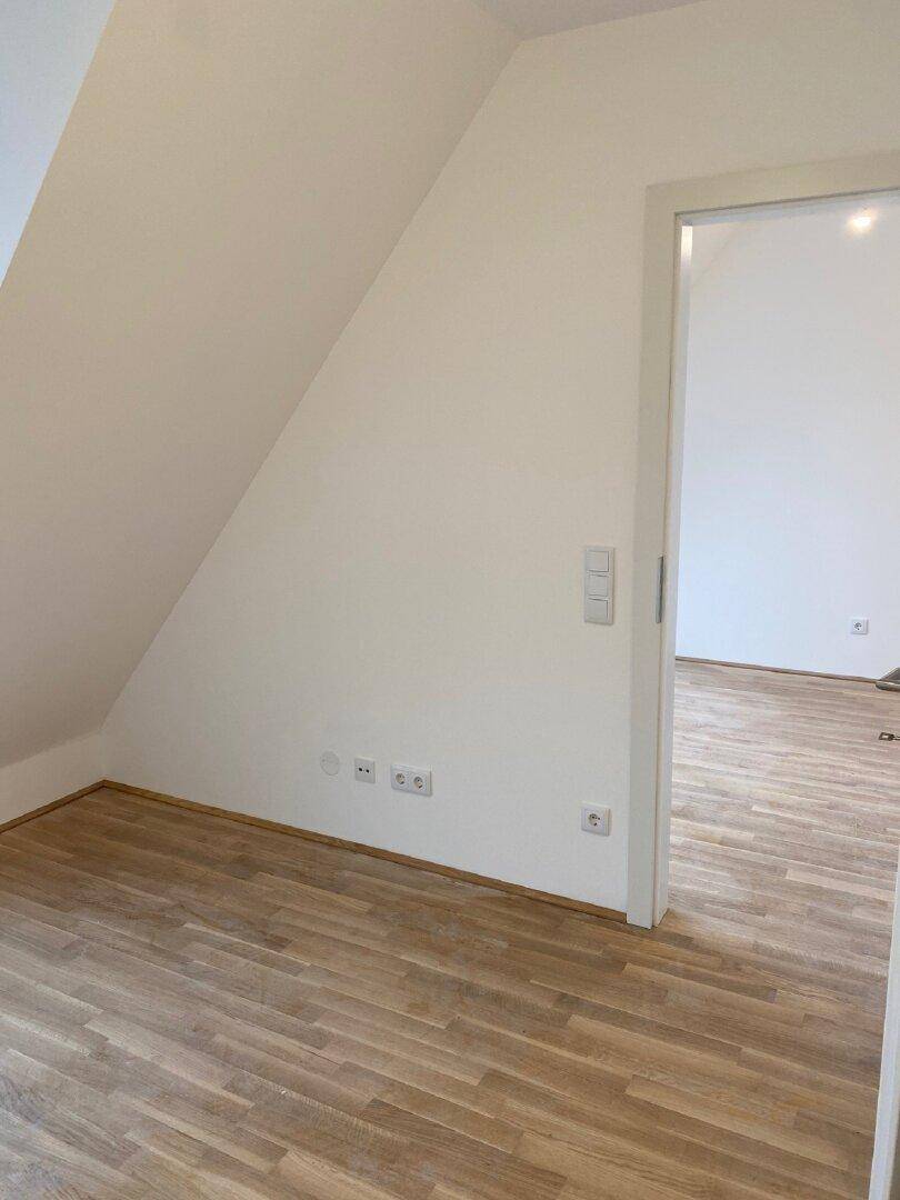 Leerer Raum mit Holzboden, weißen Wänden und einer deutlichen Dachschräge, bereit zum Einrichten.