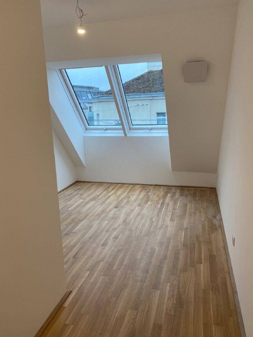 Helles Schlafzimmer mit Holzboden, Dachschräge und zwei Dachfenstern für viel Tageslicht.