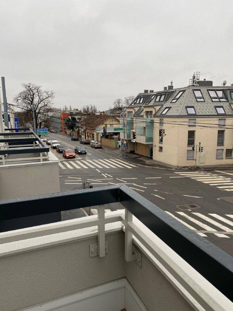 Weitblick vom Balkon auf eine belebte Straßenkreuzung mit Gebäuden und Fahrzeugen unter bewölktem Himmel.