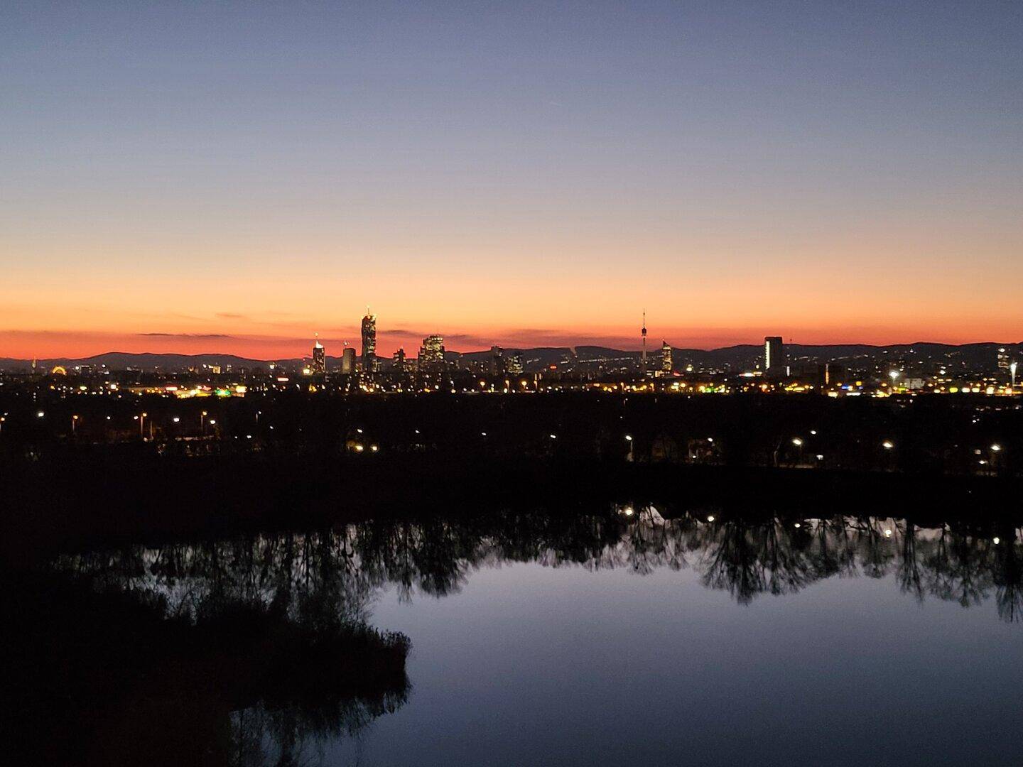 Beeindruckender Panoramablick auf die beleuchtete Stadt und den See bei Sonnenuntergang.