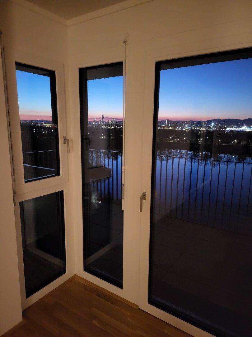 Abendlicher Blick aus dem Wohnzimmer auf die Stadtlichter und den ruhigen See.