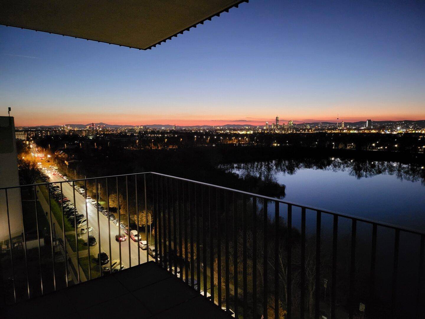 Balkon mit weitem Blick auf den See, die Straße und die Skyline der Stadt bei Dämmerung.