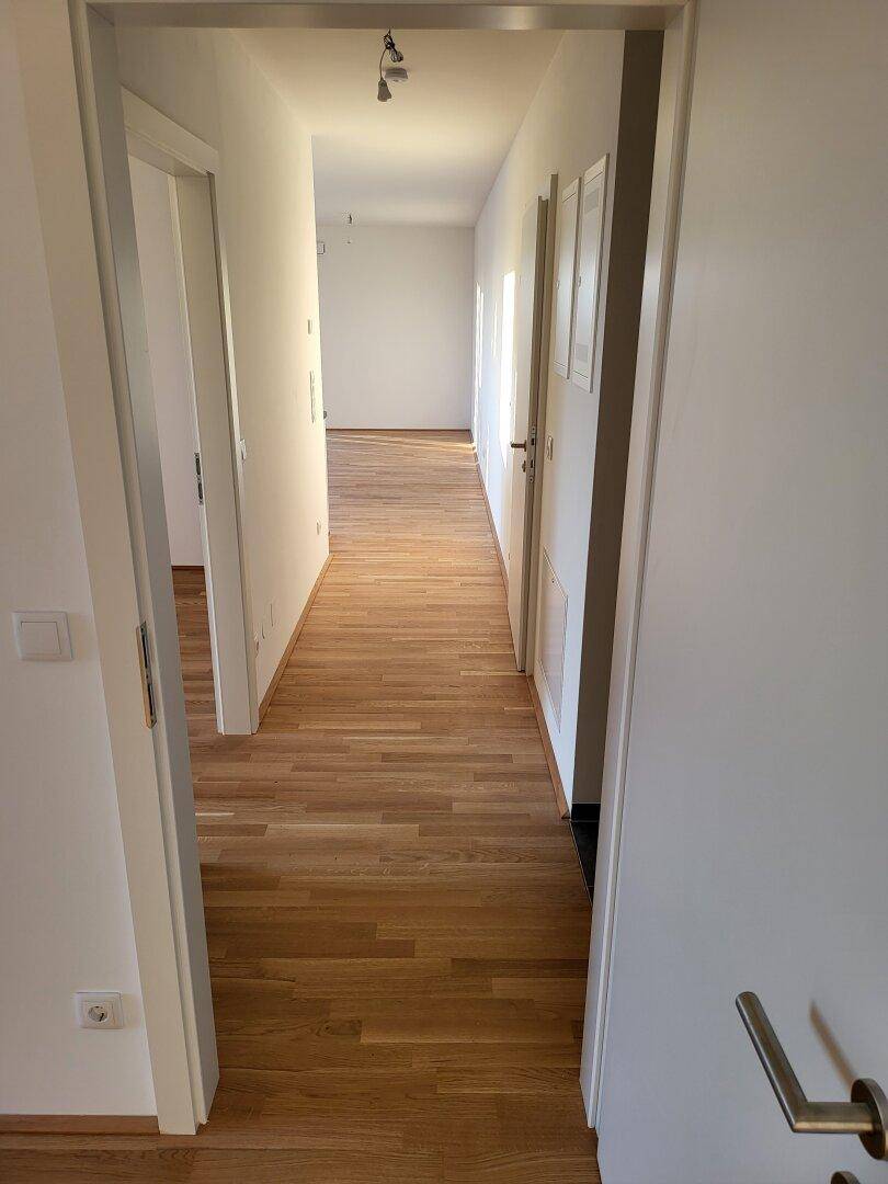 Langer, heller Flur mit Holzparkettboden, der zu den verschiedenen Zimmern führt.