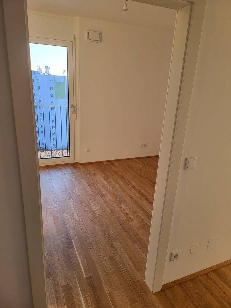 Helles Zimmer mit Parkettboden und Zugang zu einem französischen Balkon.