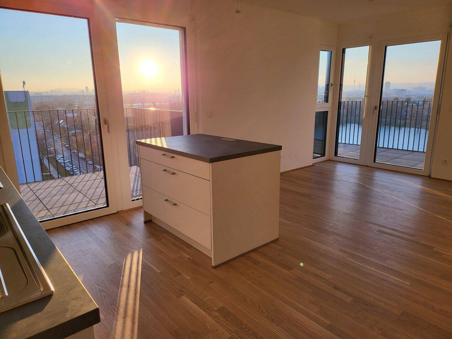 Heller Wohnbereich mit Kücheninsel und weitem Blick auf den See und die Stadt bei Sonnenuntergang.