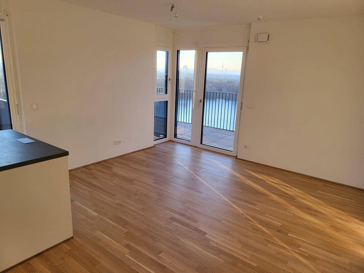 Geräumiger, heller Wohnraum mit Parkettboden und Panoramafenstern mit Seeblick.