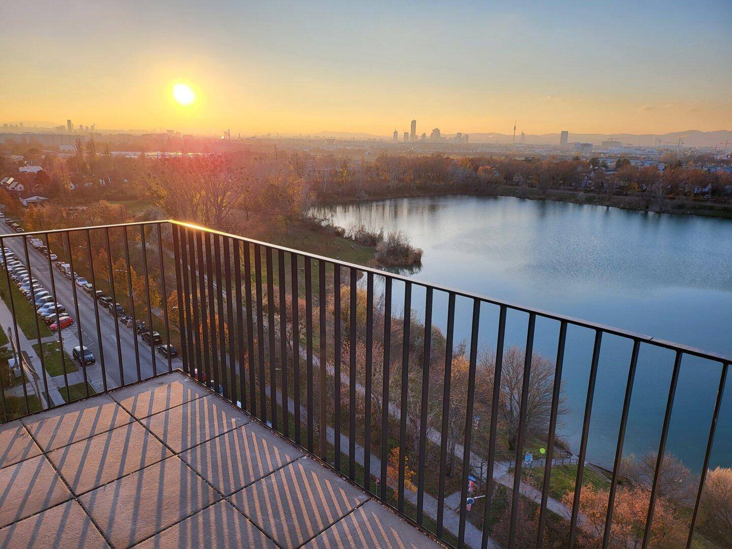 Sonniger Balkon mit Fliesenboden und Geländer, mit Panoramablick auf den See und die Stadt.