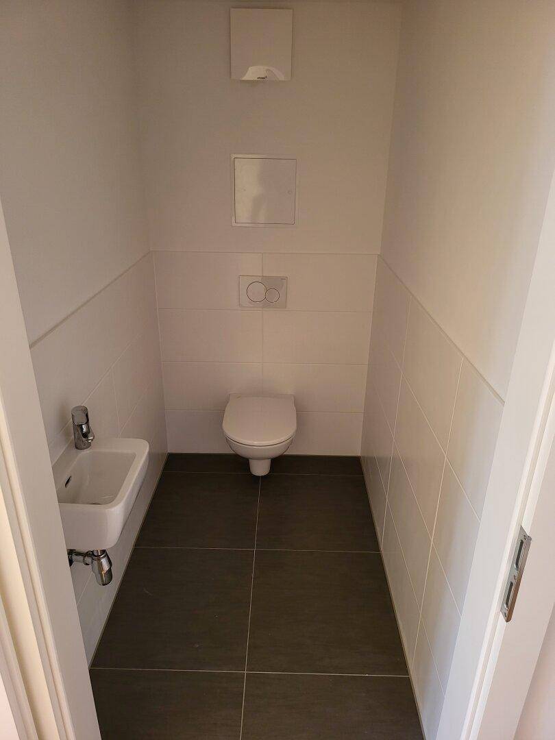 Separates Gäste-WC mit wandhängender Toilette und kleinem Handwaschbecken.