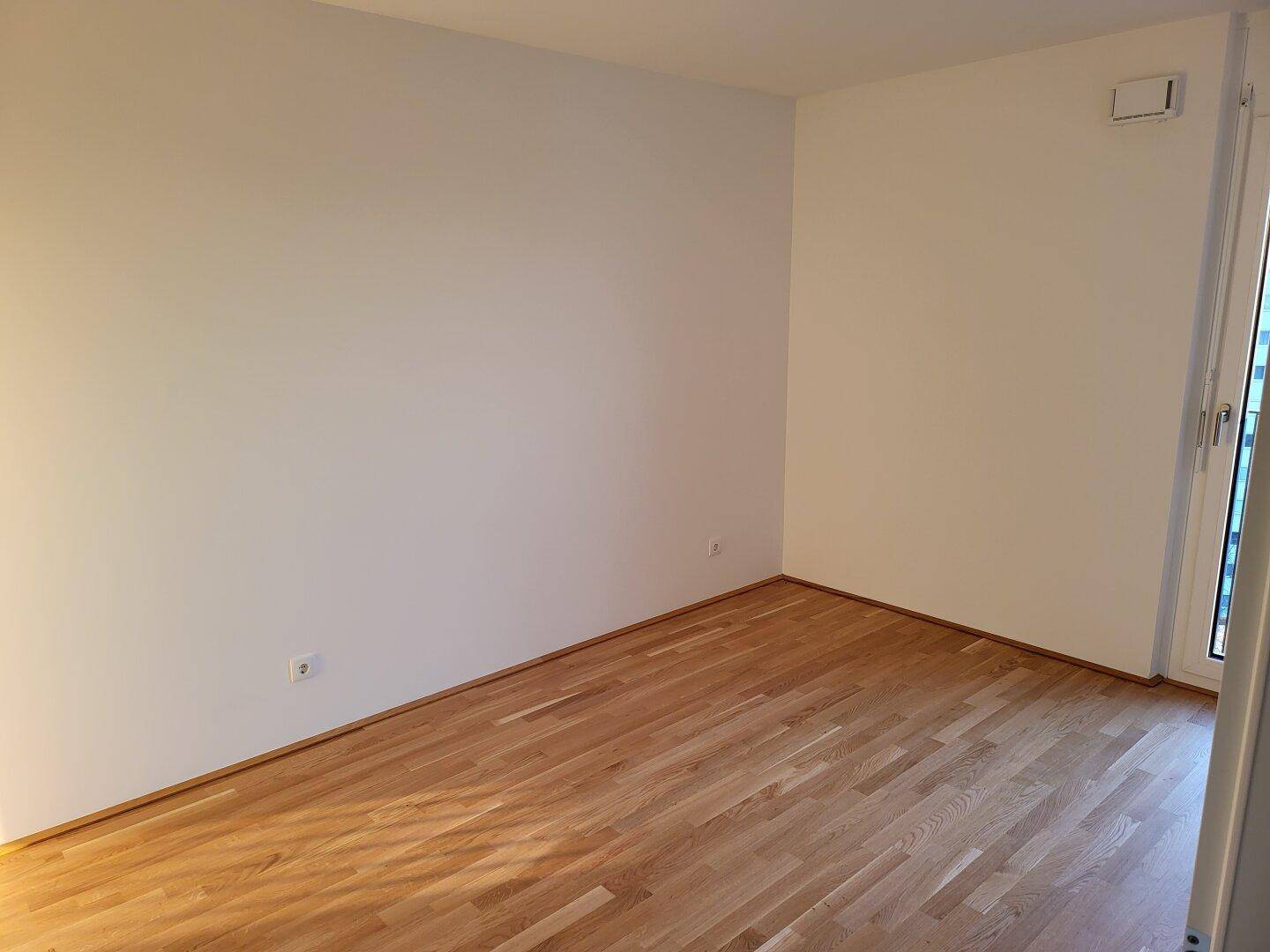 Leeres Zimmer mit hellem Parkettboden und weißen Wänden, bereit zur individuellen Gestaltung.