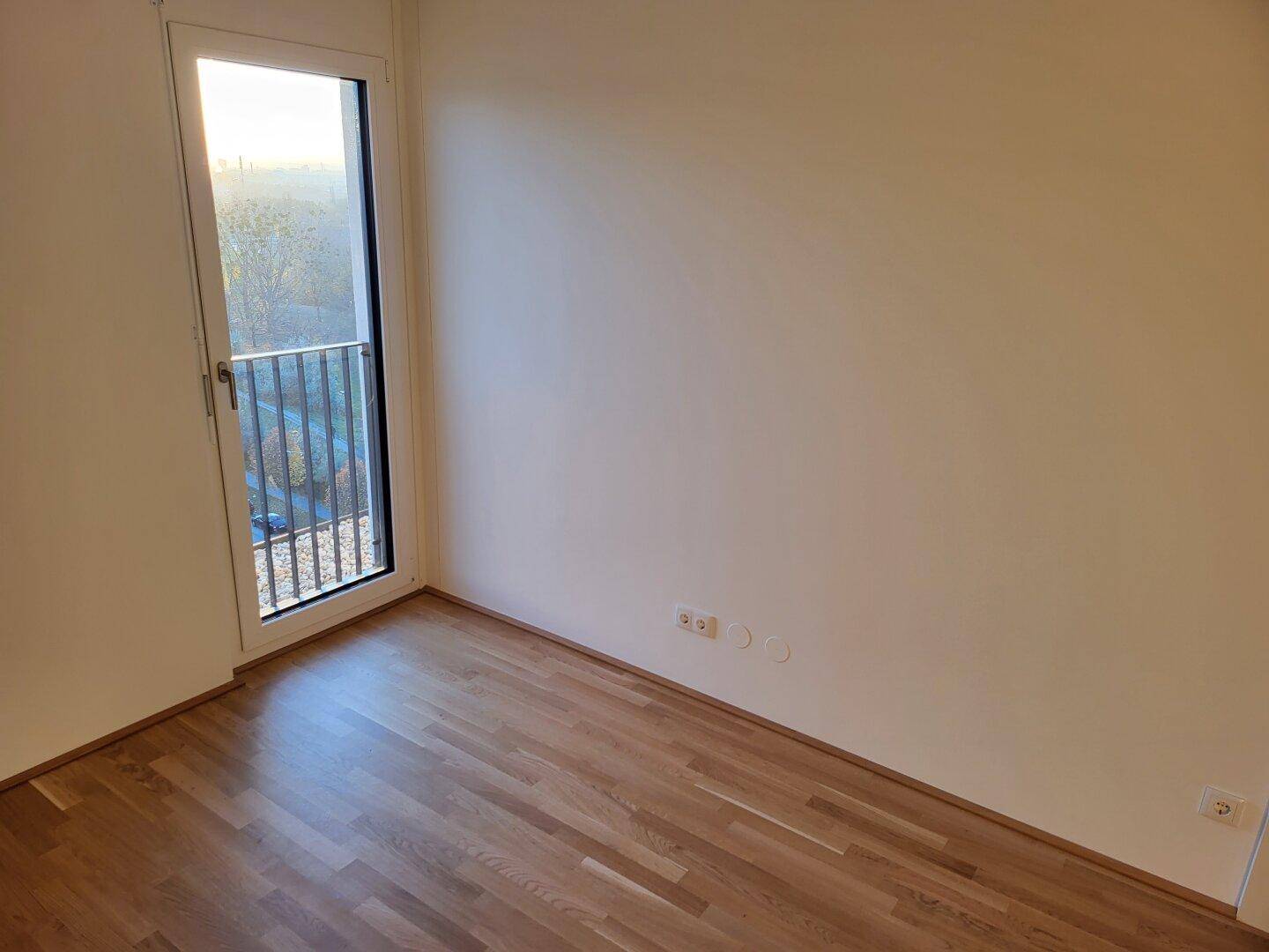 Helles Schlafzimmer mit Parkettboden und einem französischen Balkon für frische Luft.