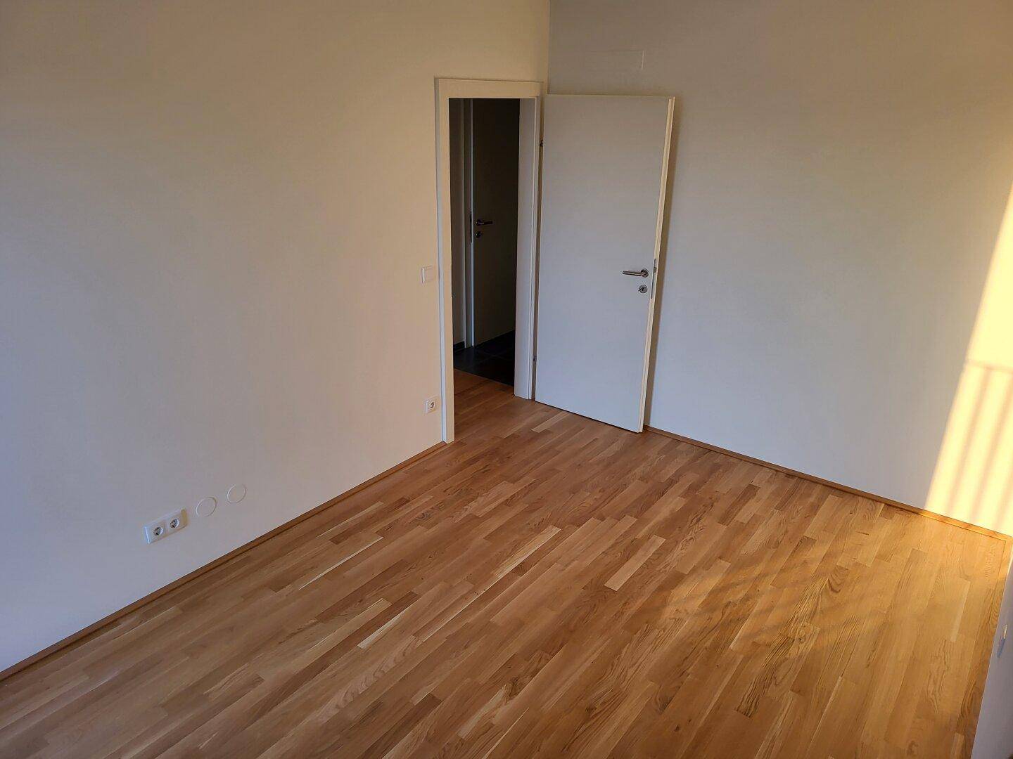 Geräumiges Zimmer mit Parkettboden und offener Tür, die zu einem weiteren Raum führt.