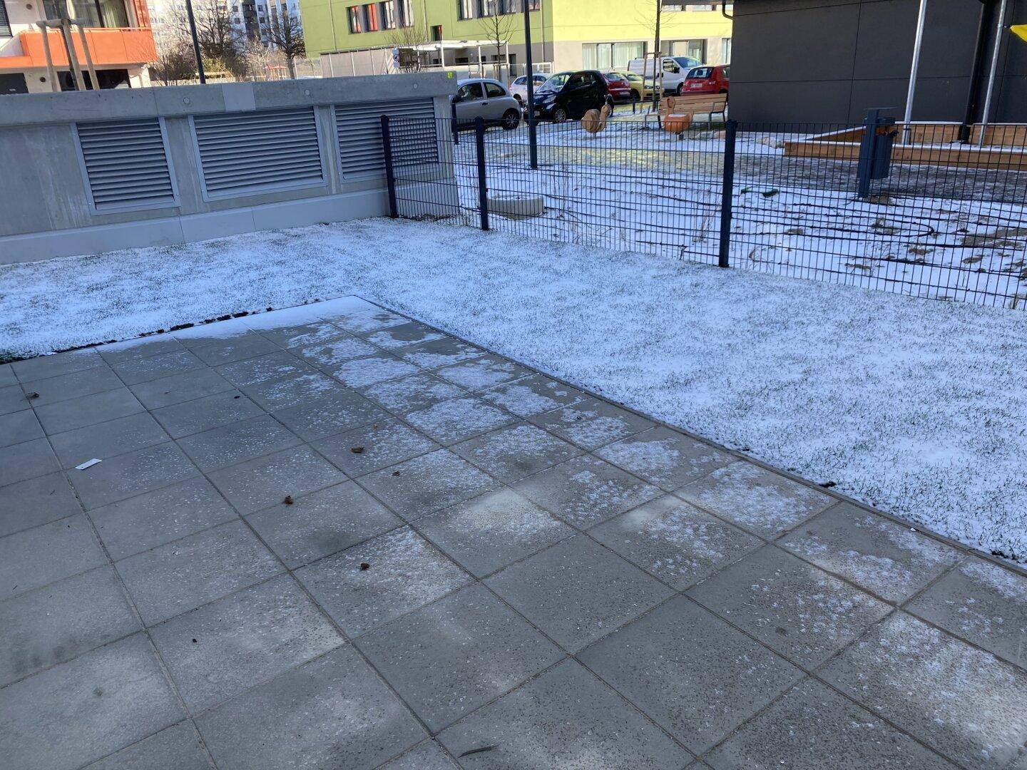 Kleiner Gartenbereich mit Rasen und gepflasterter Terrasse, umgeben von einem Zaun.