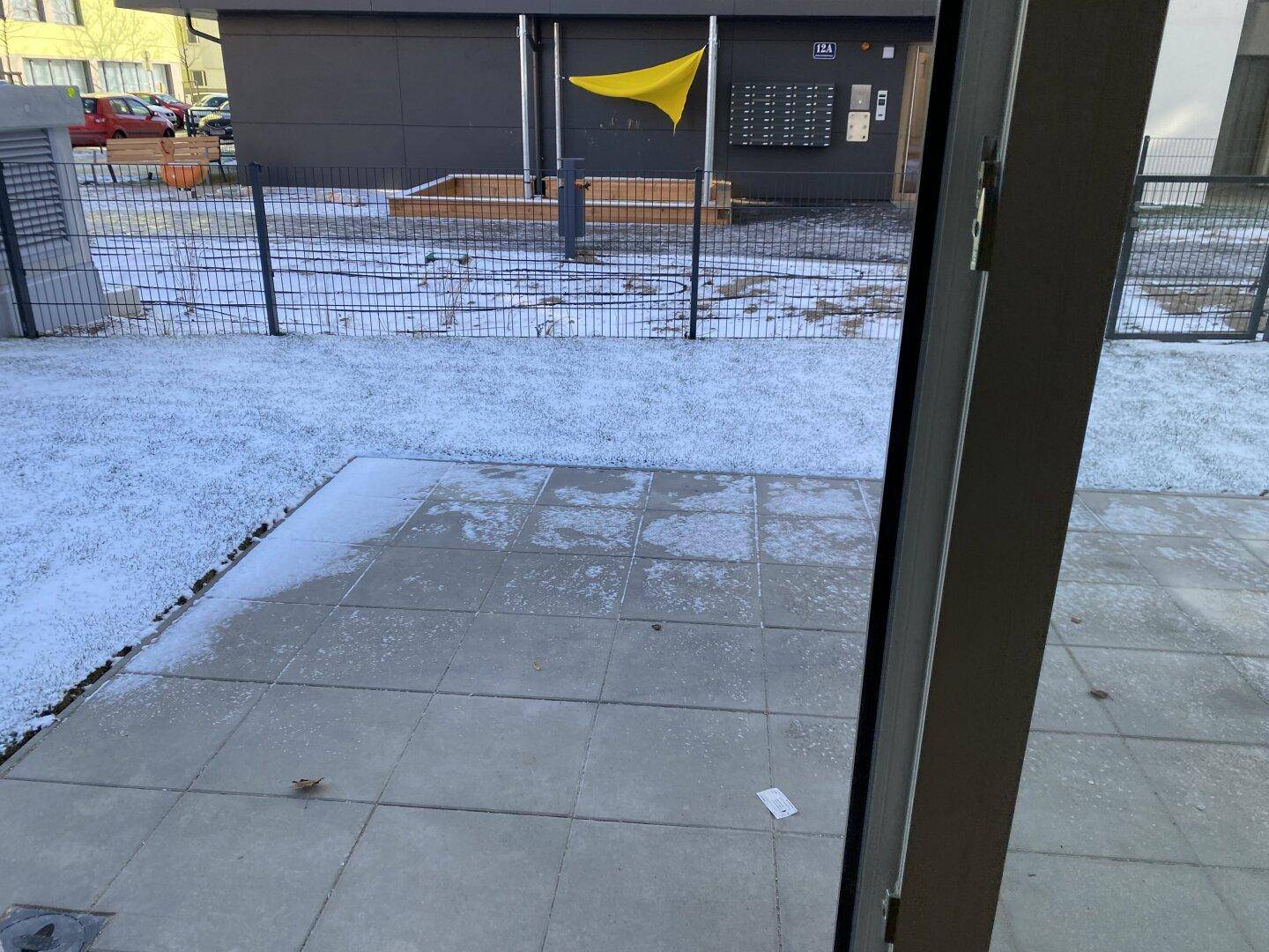 Gepflasterte Terrasse mit Schneeauflage und Blick auf den Gemeinschaftsbereich des Gebäudes.