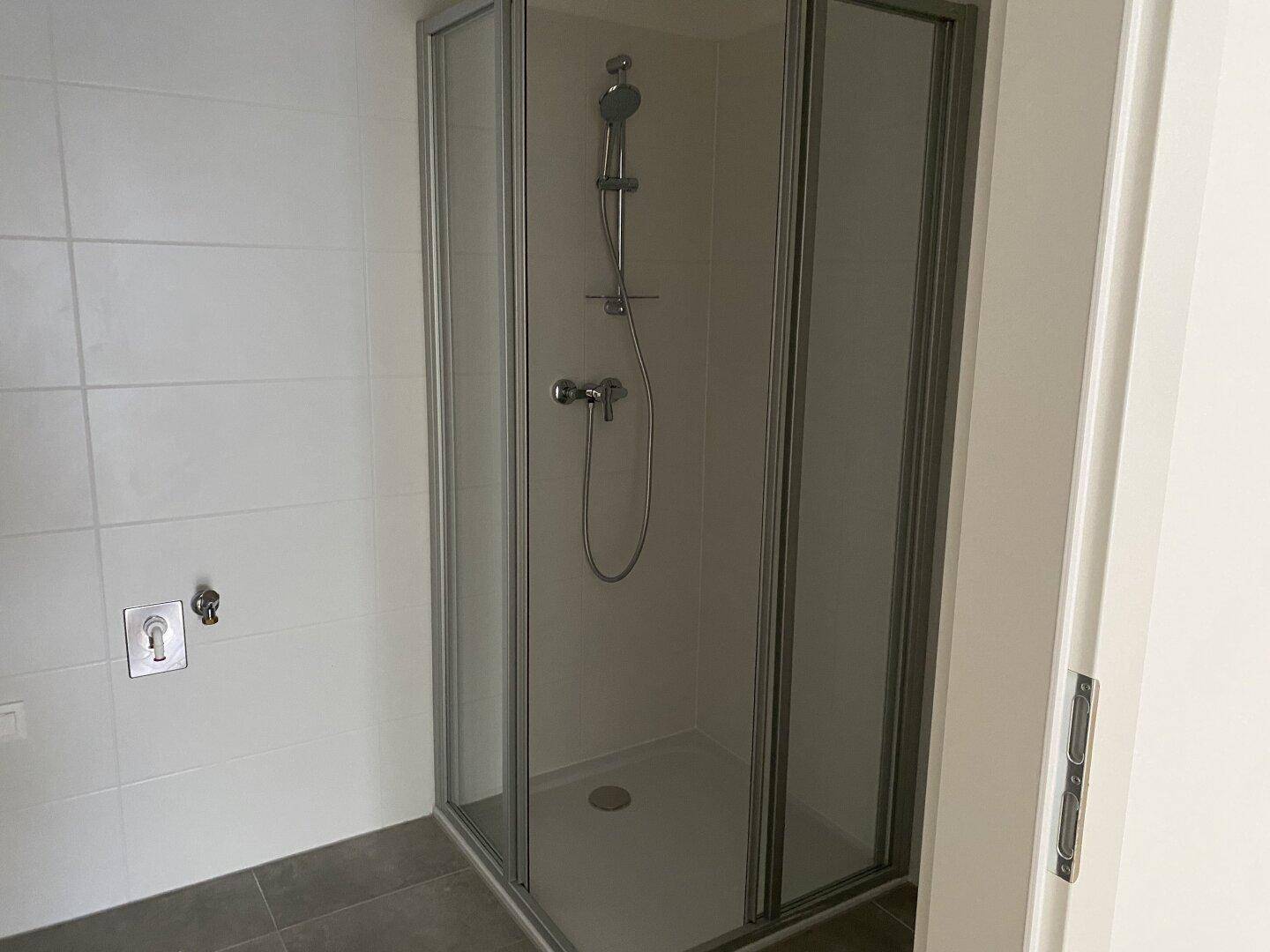 Modernes Badezimmer mit Duschkabine und weißen Fliesen, bereit zur Nutzung.