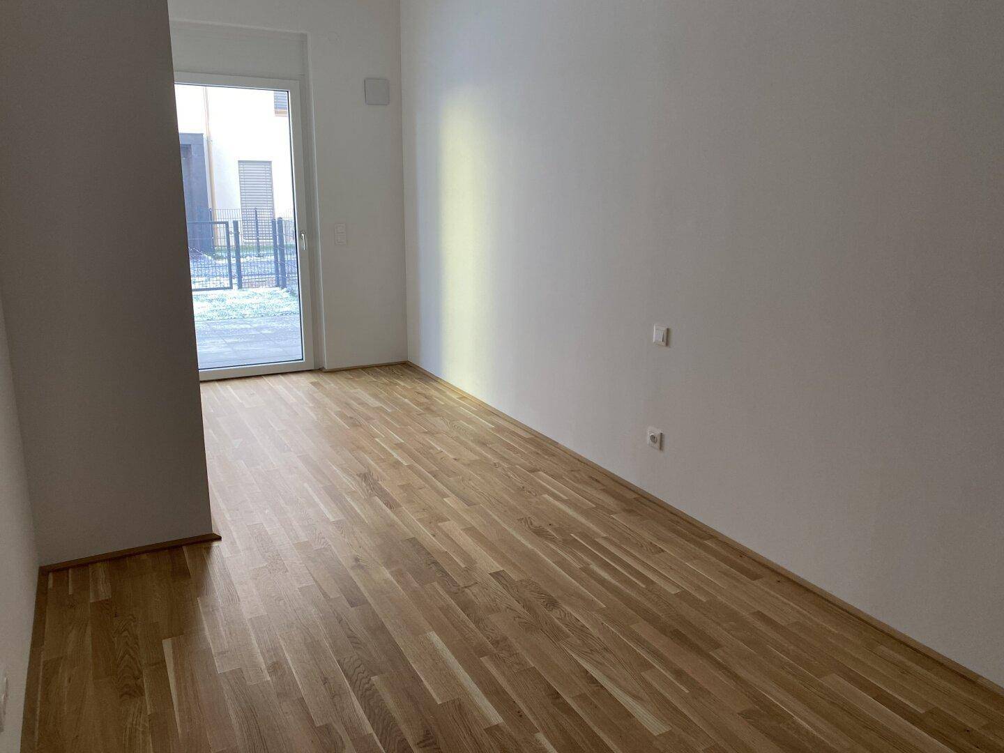 Heller Wohnbereich mit Parkettboden und Zugang zum Außenbereich, ideal für natürliche Belichtung.