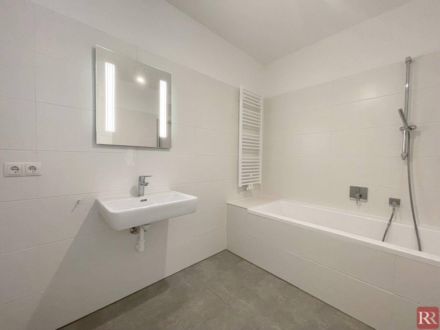 Modernes Badezimmer mit Badewanne, Waschtisch und beheiztem Handtuchhalter in hellen Fliesen.