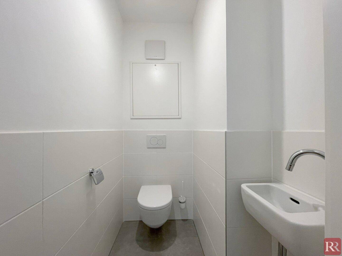 Separates Gäste-WC mit wandhängender Toilette und kleinem Handwaschbecken.