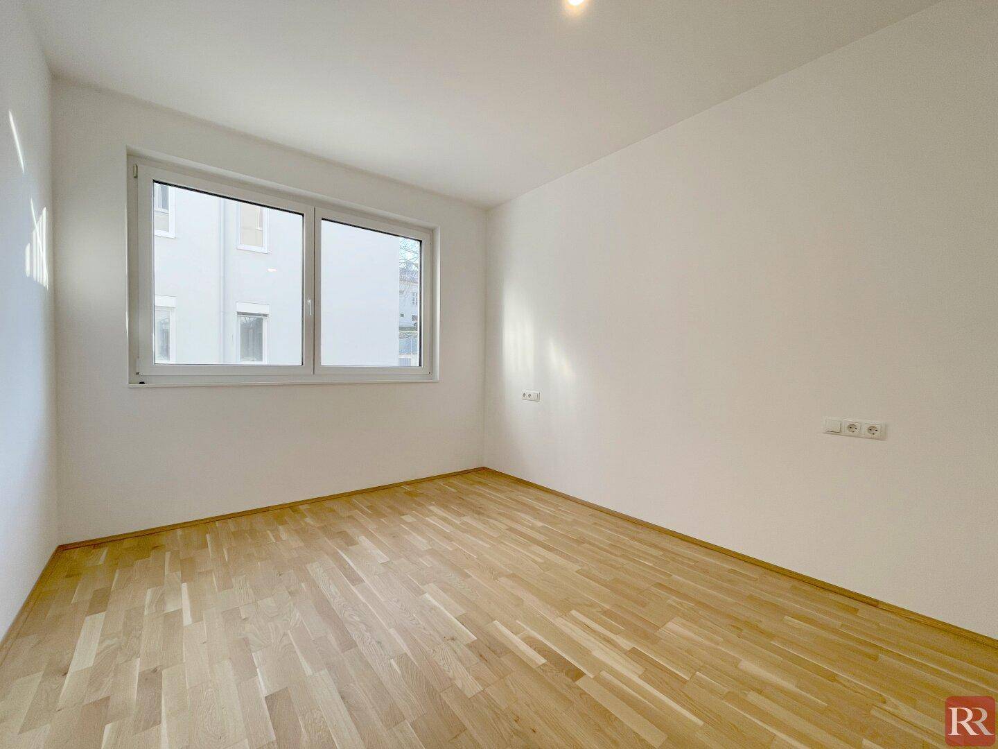 Helles Schlafzimmer mit Parkettboden und großem Fenster, bietet viel Tageslicht.