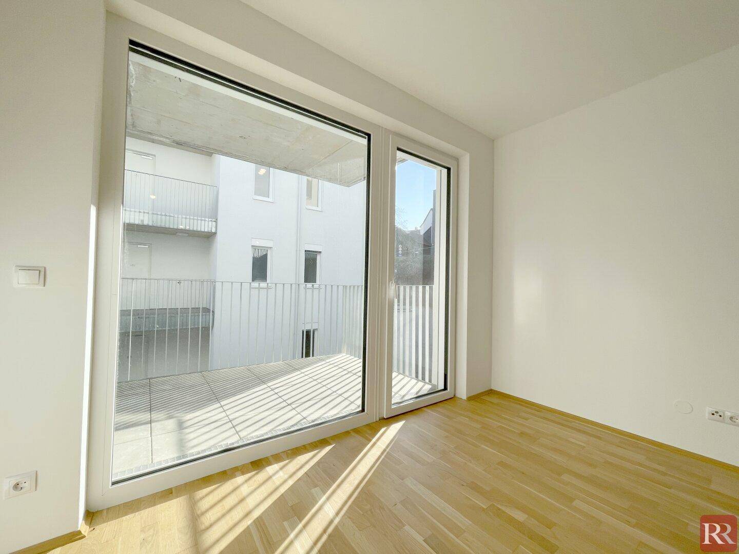 Lichtdurchflutetes Schlafzimmer mit Zugang zu einem Balkon und hellem Parkettboden.