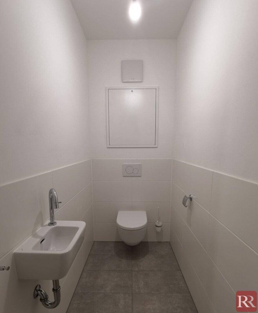 Modernes Gäste-WC mit Wand-WC, kleinem Waschbecken und grauen Bodenfliesen.
