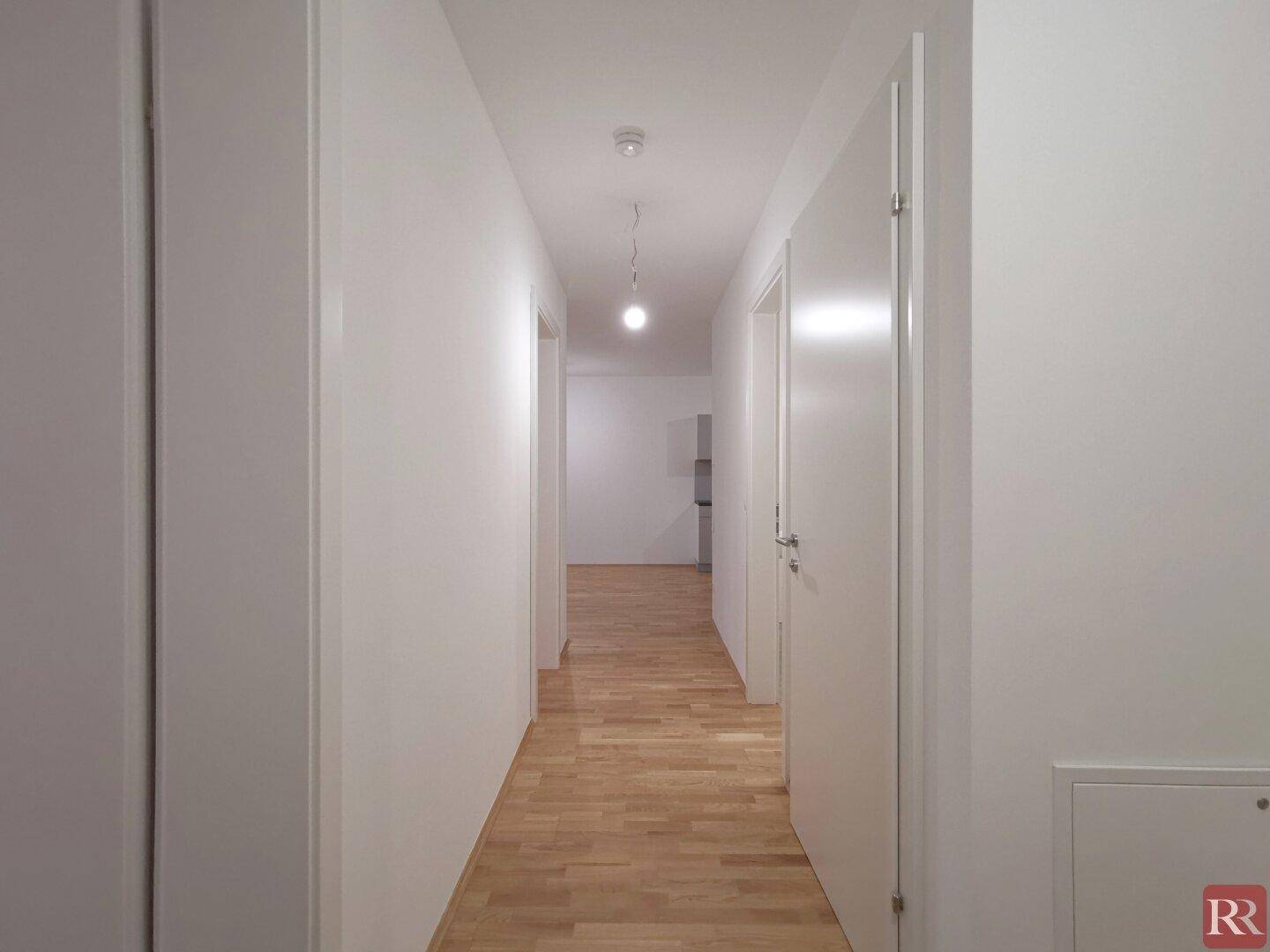 Langer, heller Flur mit Parkettboden und weißen Wänden, der zu weiteren Räumen führt.