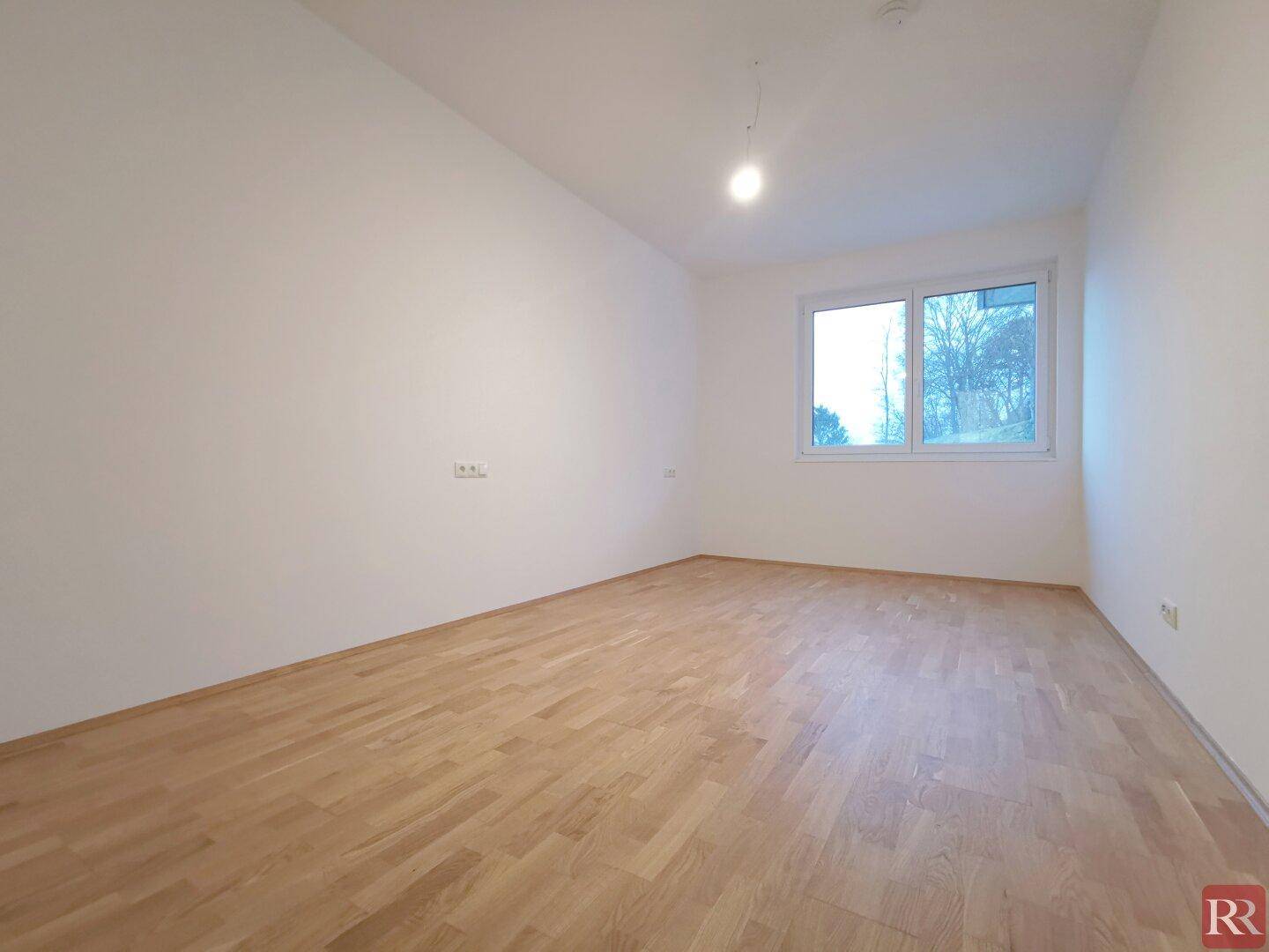 Geräumiges, helles Schlafzimmer mit Parkettboden und einem großen Fenster, unmöbliert.