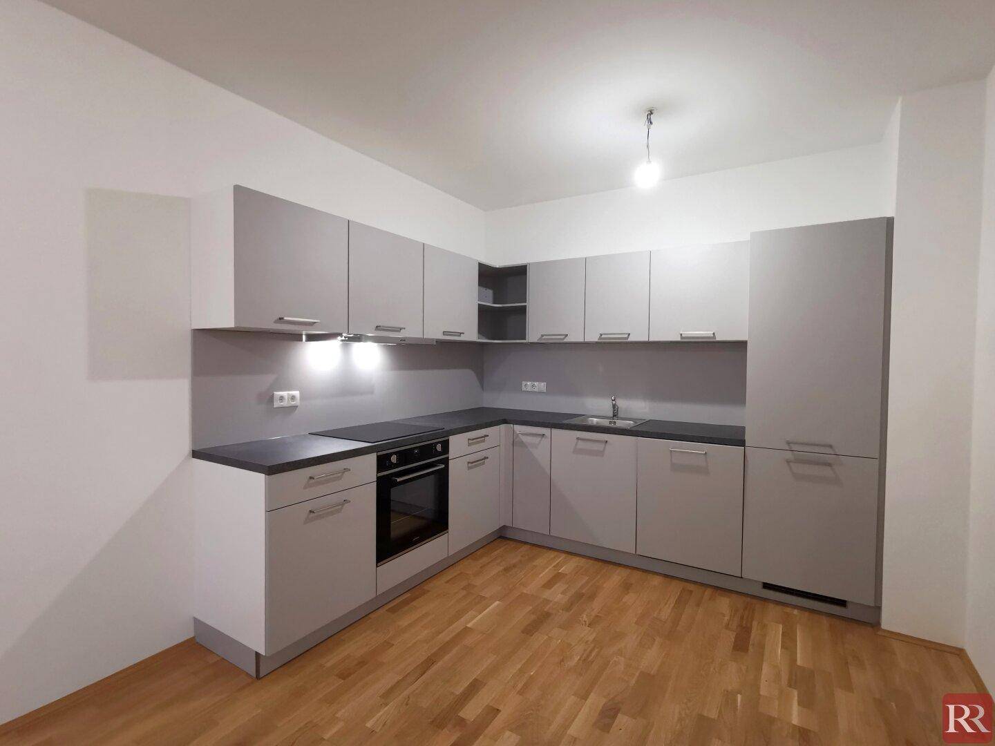 Neue, moderne Einbauküche in Grau mit integrierten Geräten und Parkettboden.