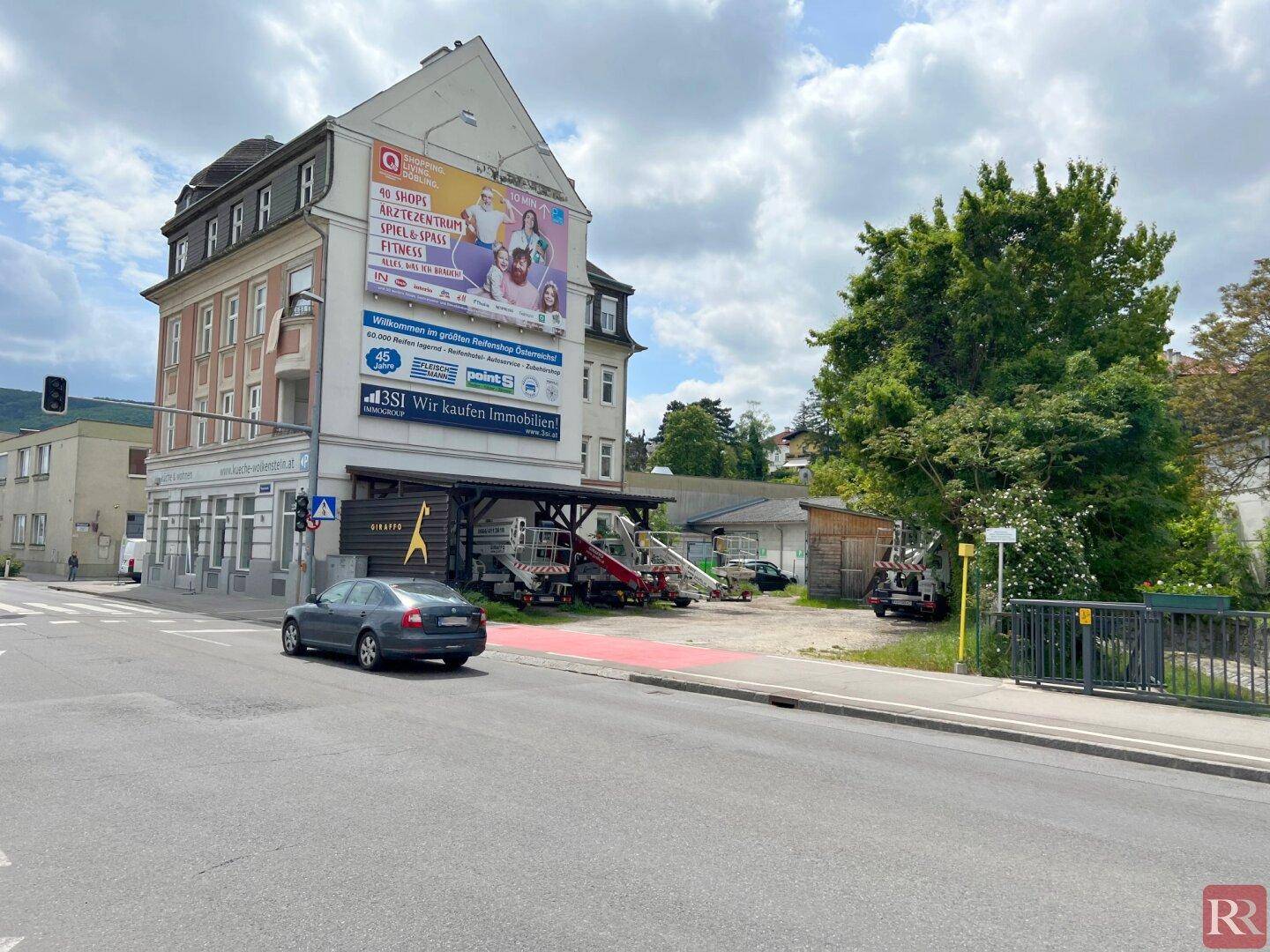 Gebäude an einer Straßenecke mit Werbebanner und angrenzendem unbebautem Grundstück.