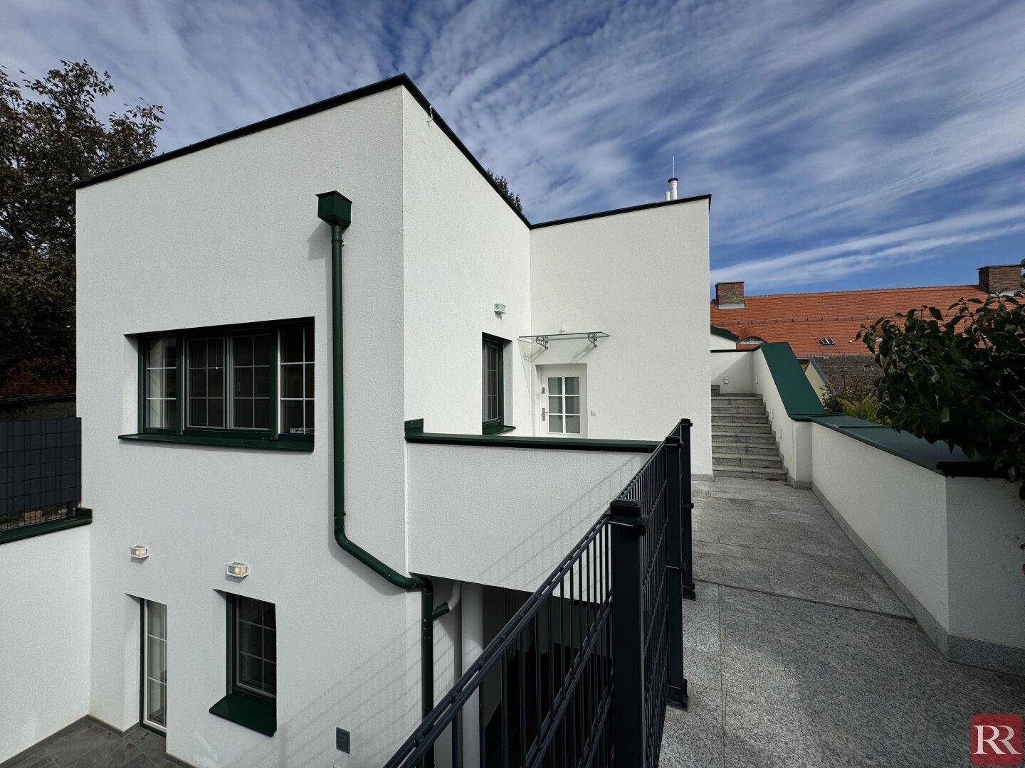 Moderne Architektur mit weißer Fassade, dunklen Fenstern und Außentreppe.