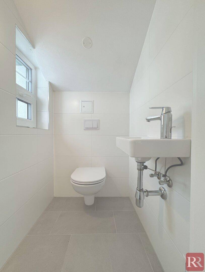 Praktisches Gäste-WC mit wandhängender Toilette, kleinem Waschbecken und Fenster.