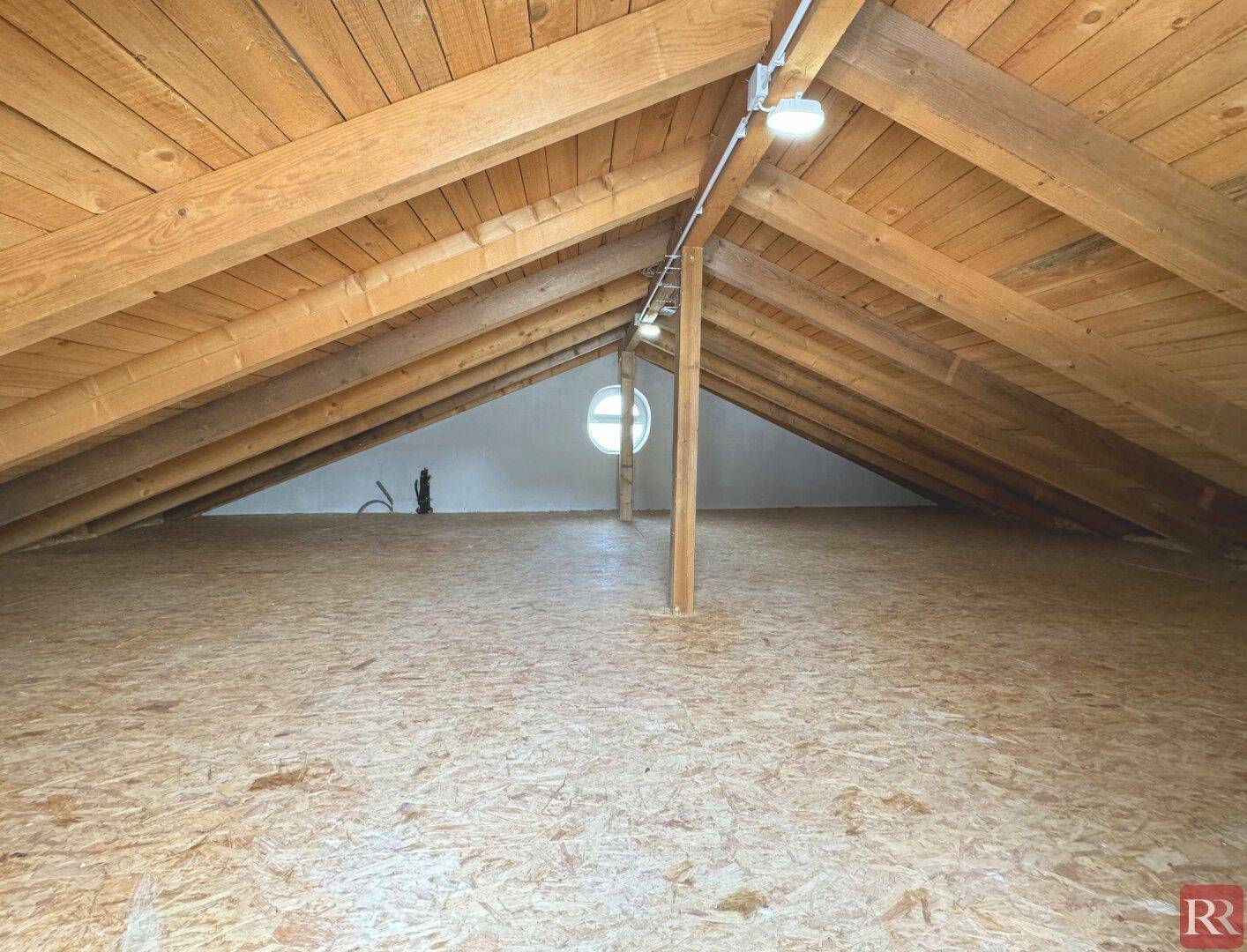 Geräumiger Dachboden mit sichtbaren Holzbalken und einem runden Fenster.