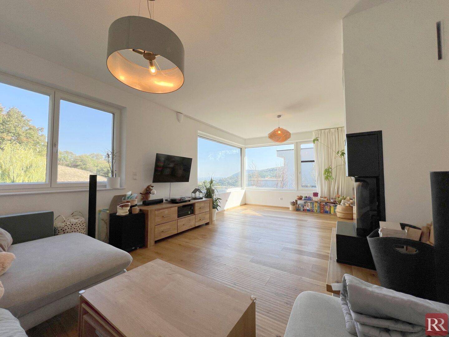 Helles Wohnzimmer mit großen Fenstern, Holzboden und Blick ins Grüne.