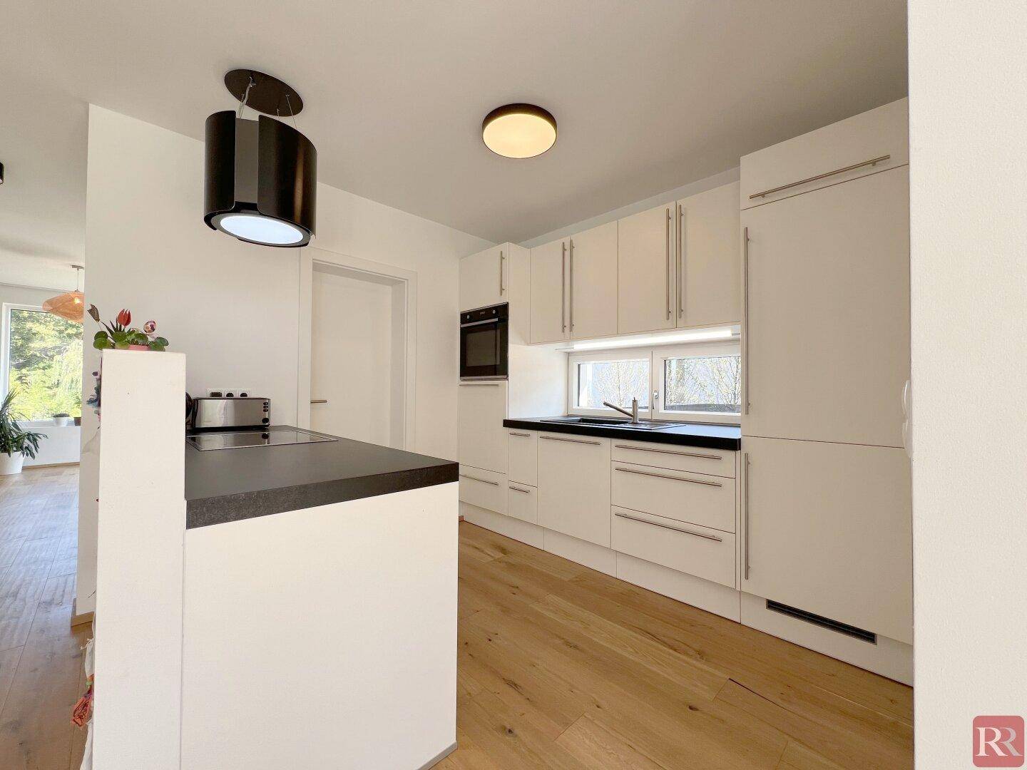 Moderne Einbauküche mit weißen Schränken, dunkler Arbeitsplatte und Holzboden.