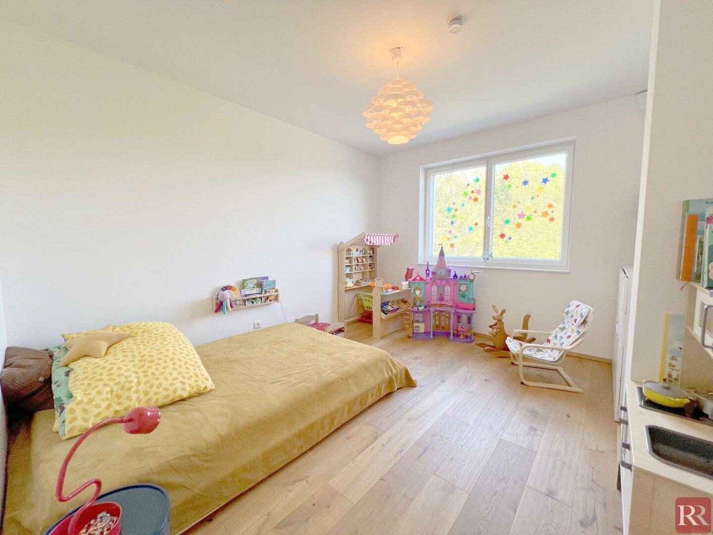 Kinderzimmer mit Holzboden, hellen Wänden und viel Tageslicht durch das Fenster.