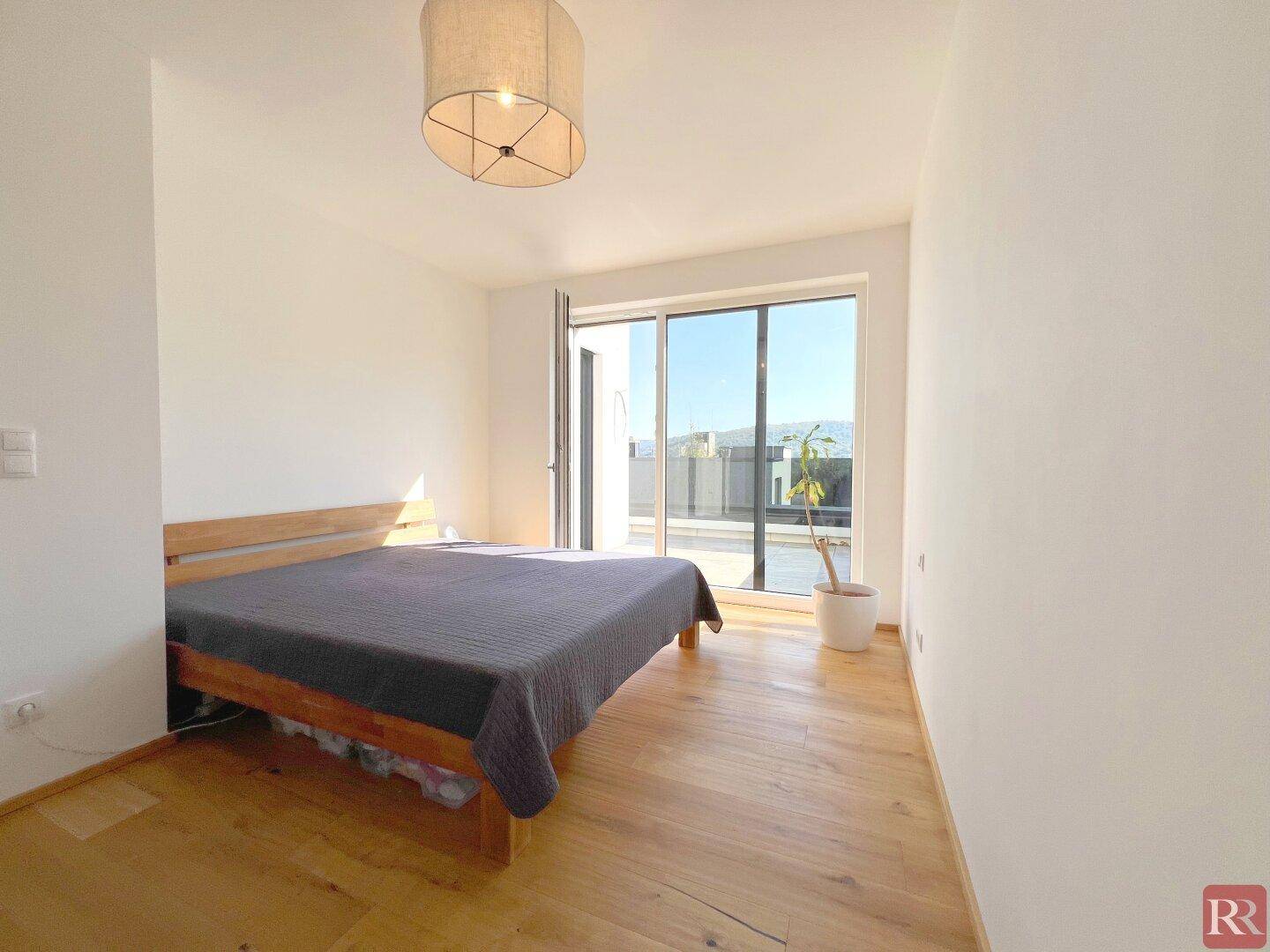 Schlafzimmer mit Holzboden und direktem Zugang zu einer sonnigen Terrasse.