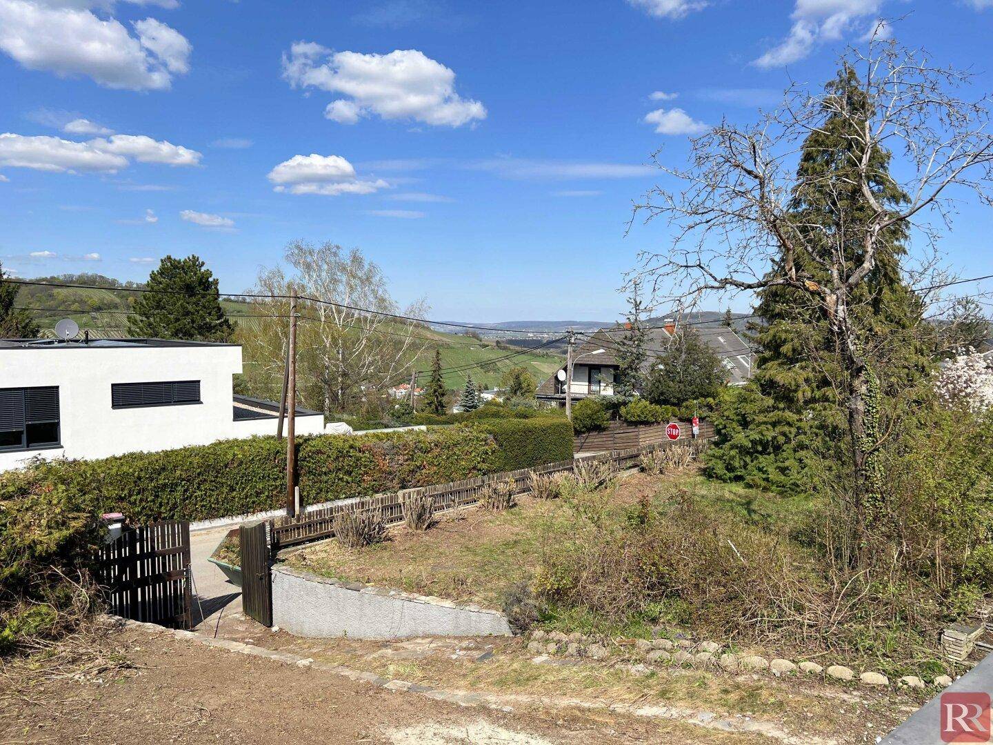 Panoramablick über die hügelige Landschaft mit verstreuten Häusern und viel Grün unter strahlendem Himmel.