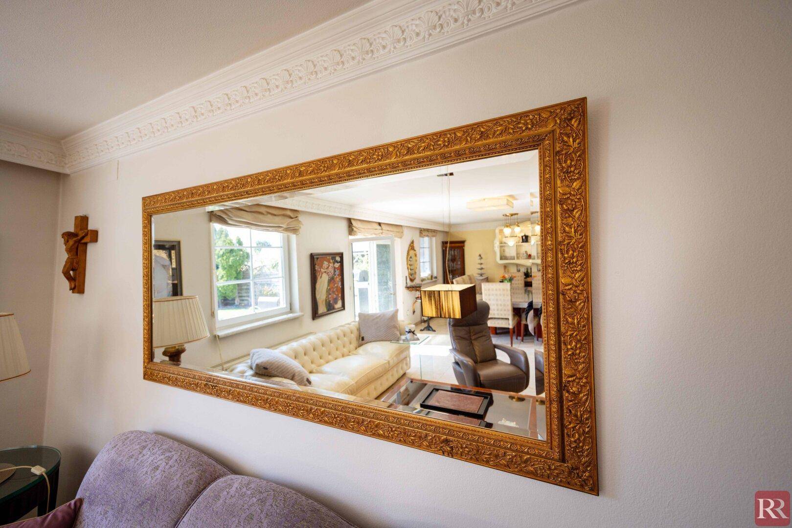 Detailaufnahme eines großen, verzierten Spiegels im Wohnzimmer, der den Raum reflektiert.