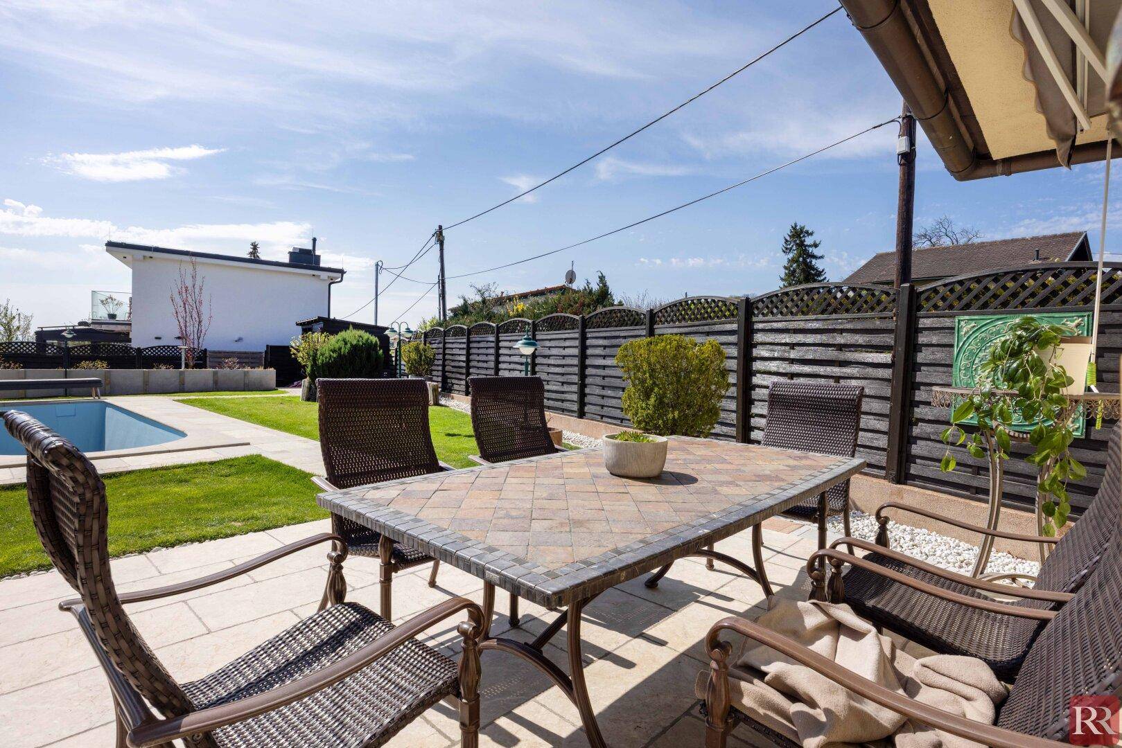 Gemütliche Terrasse mit Outdoor-Sitzgelegenheiten und Blick auf den Garten und den Poolbereich.