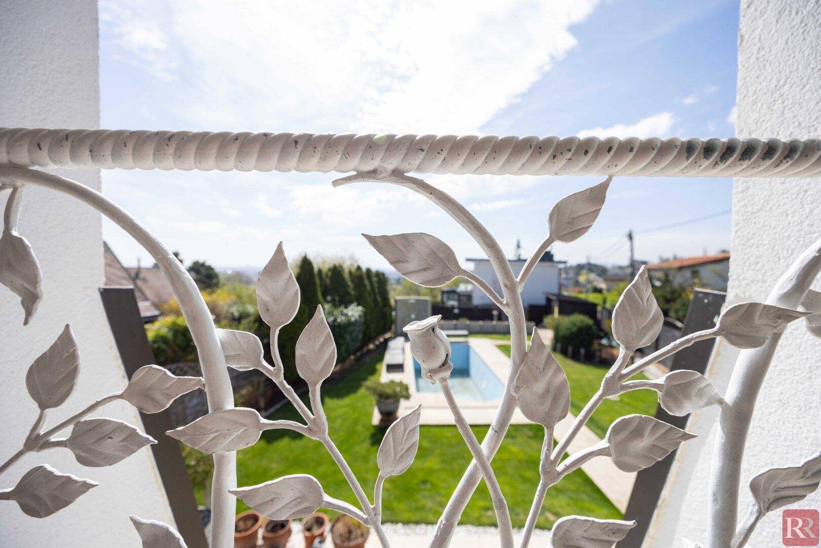 Blick vom französischen Balkon auf den Garten mit Pool und die umliegende Landschaft.