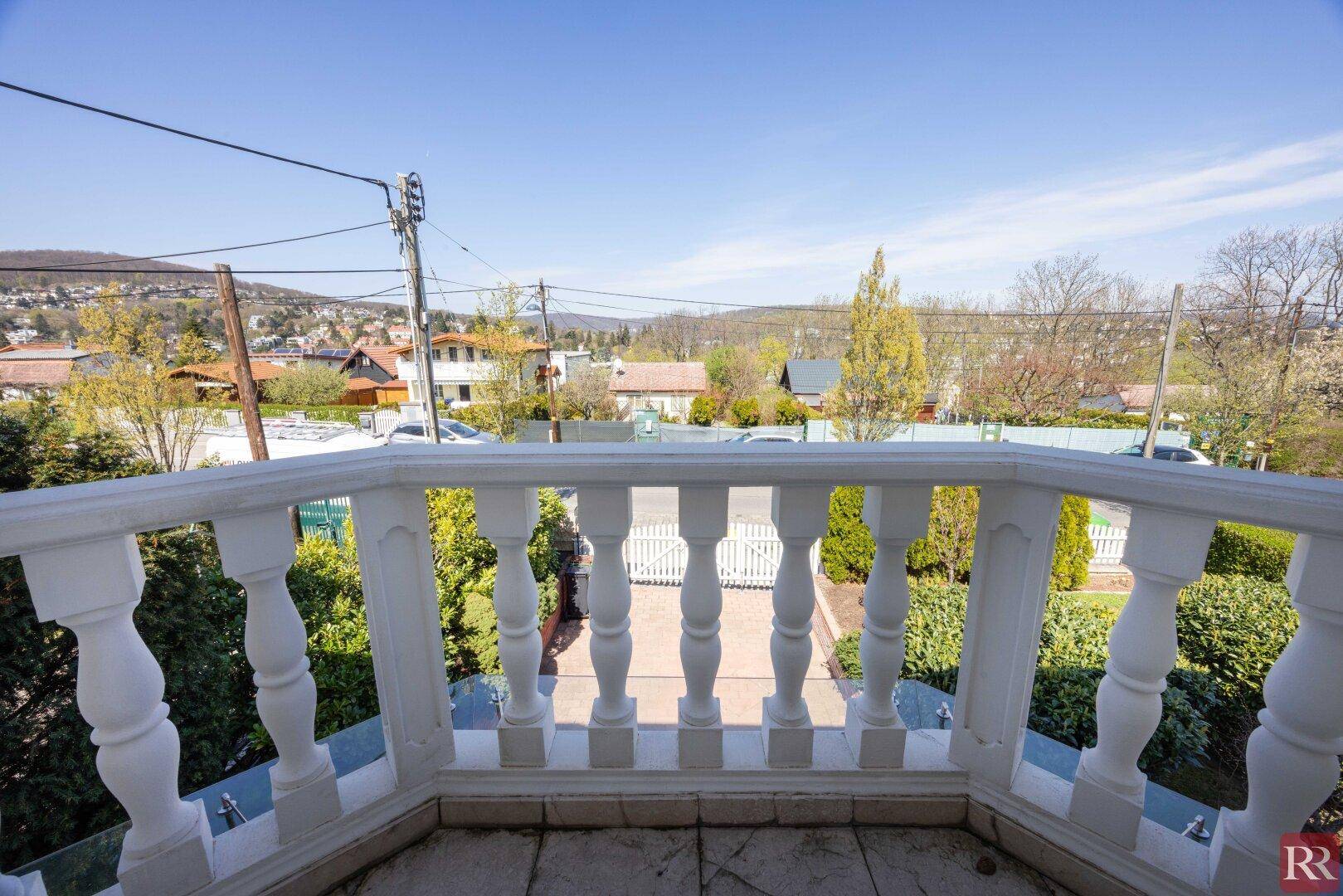 Kleiner Balkon mit weißem Geländer und Blick auf die umliegende Wohngegend und Landschaft.